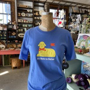 Columbia Blue short sleeve shirt with a butter lamb printed on the front in yellow, with red and black accents. The shirt reads "It's Butter in Buffalo™"