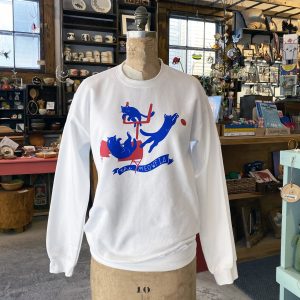 Buffalo Bills inspired shirt with the cat version of BILLS MAFIA. Sweatshirt features blue and red illustrations of cats jumping through a table, playing catch with a football and jumping over the field goal posts. Banner printed across the bottom reads "The Meowfia". Sweatshirt is white.